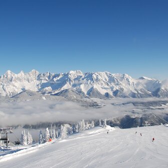 View of snowy slope, skiers, and impressive mountain panorama in the background.