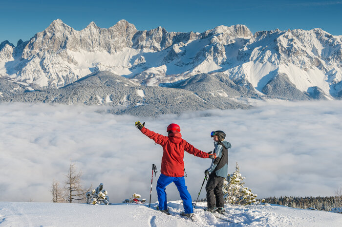 Two skiers at Reiteralm looking at a sea of fog and snow-covered mountains. | © Lorenz Masser