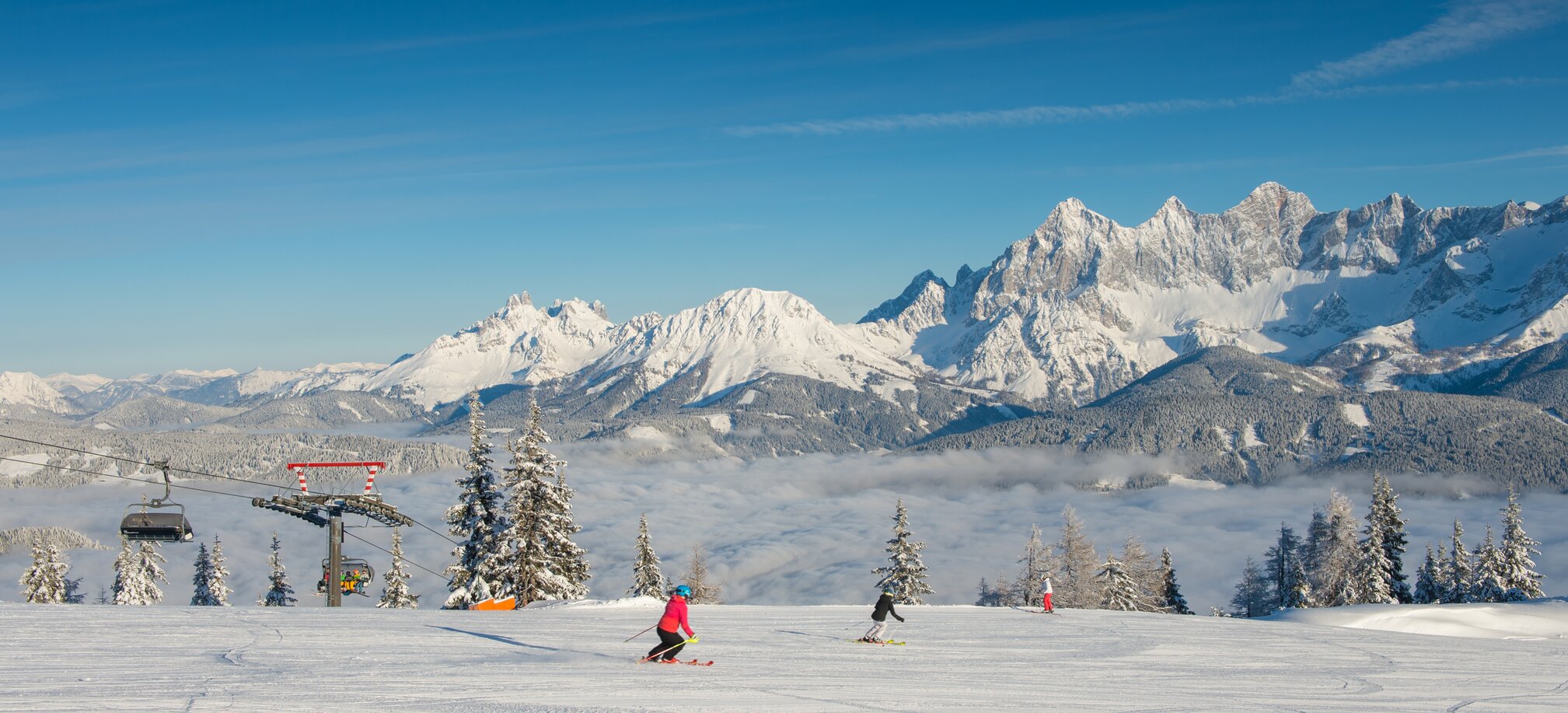 Two skiers on groomed slope at Reiteralm, with snow-covered Dachstein mountains behind. | © Lorenz Masser