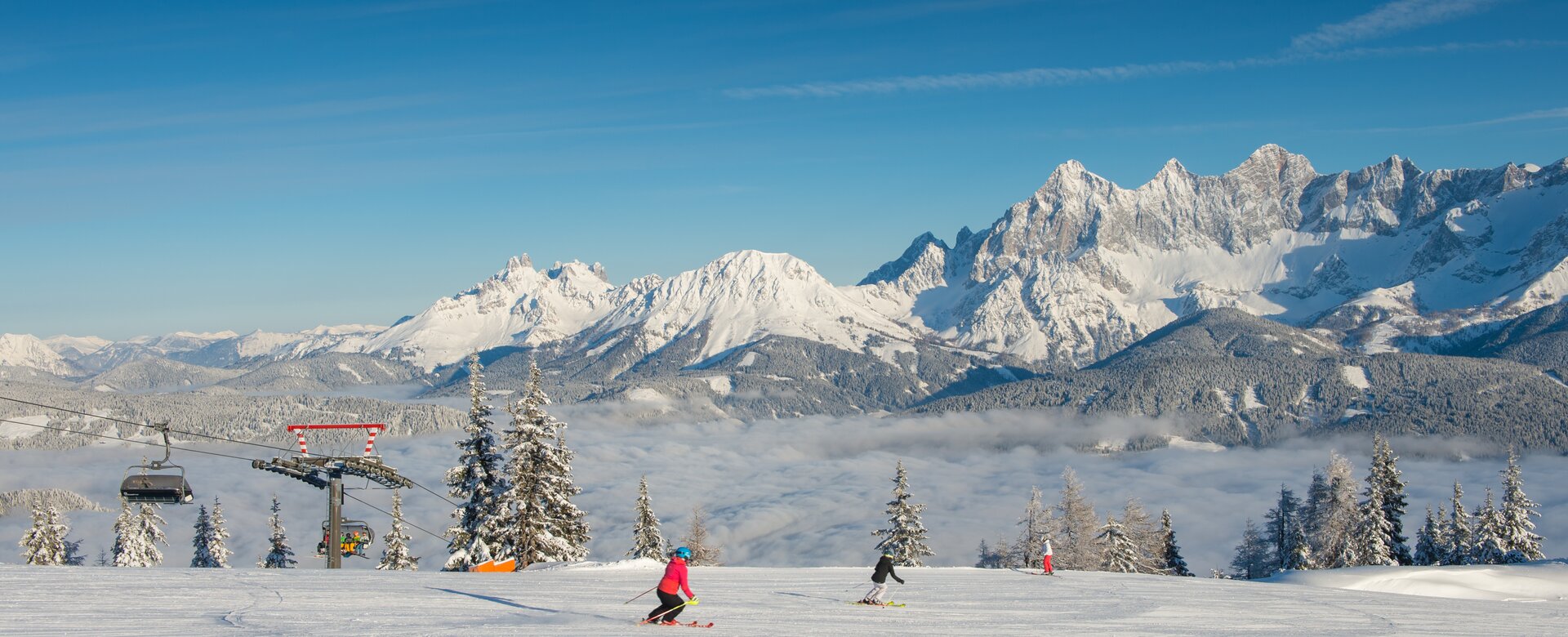 Two skiers on groomed slope at Reiteralm, with snow-covered Dachstein mountains behind. | © Lorenz Masser