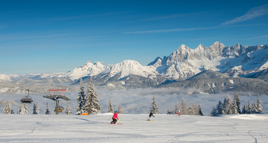 Two skiers on groomed slope at Reiteralm, with snow-covered Dachstein mountains behind. | © Lorenz Masser