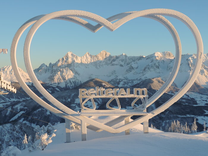 Steirerherz sculpture at Reiteralm with snow-covered Dachstein mountains in the background.