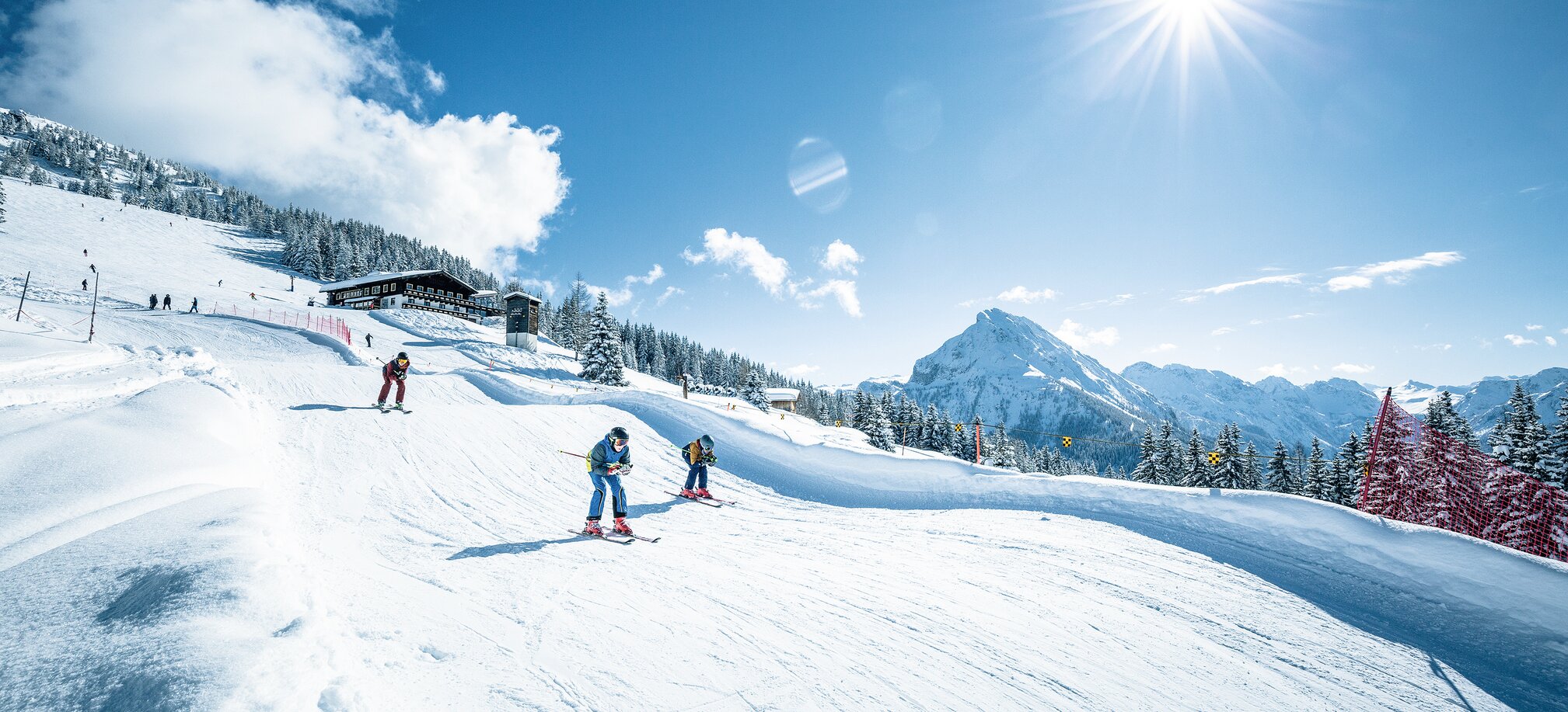 Skiers on the skicross run with sunshine, snow, hills and mountain panorama in the background | © Shuttleberg