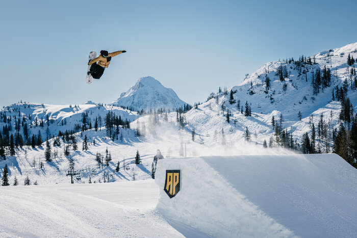A snowboarder has jumped over a jump made of snow and makes a turn and a grab in the air | © MRochrbacher
