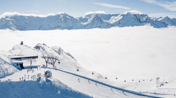 The mountain station of a cable car with skiers and snowboarders and the valley covered in high fog. | © Gasteinertal Tourismus GmbH, Christoph Oberschneider