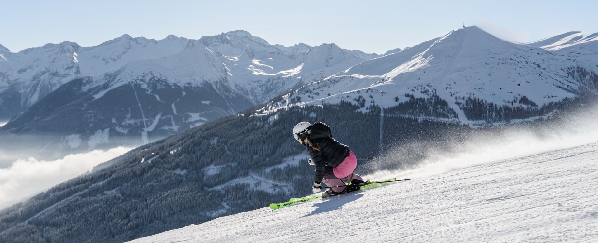Skier carving on a slope with view of snowy forests and high mountains | © Simon Hutter