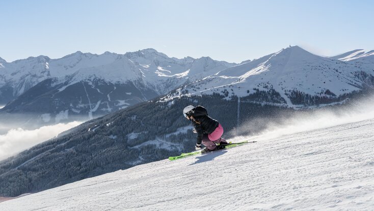 Skier carving on a slope with view of snowy forests and high mountains | © Simon Hutter