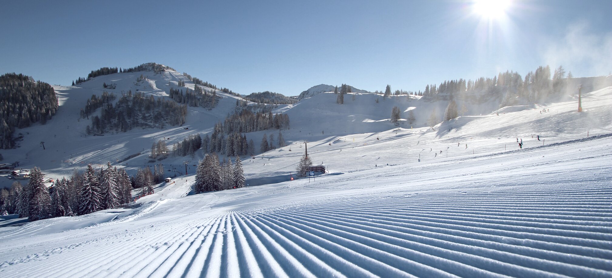 Perfectly groomed ski slopes at Alpendorf ski area with sun, snow and mountains