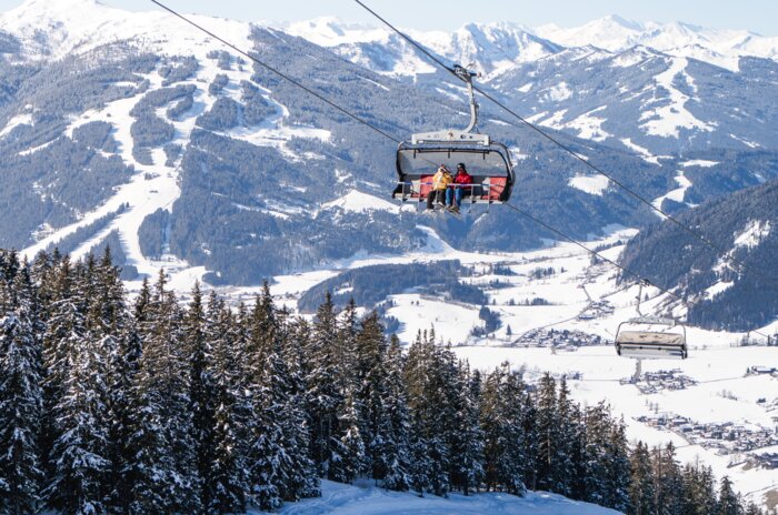 A chairlift with four people floats above slope with a view of snow-covered mountains