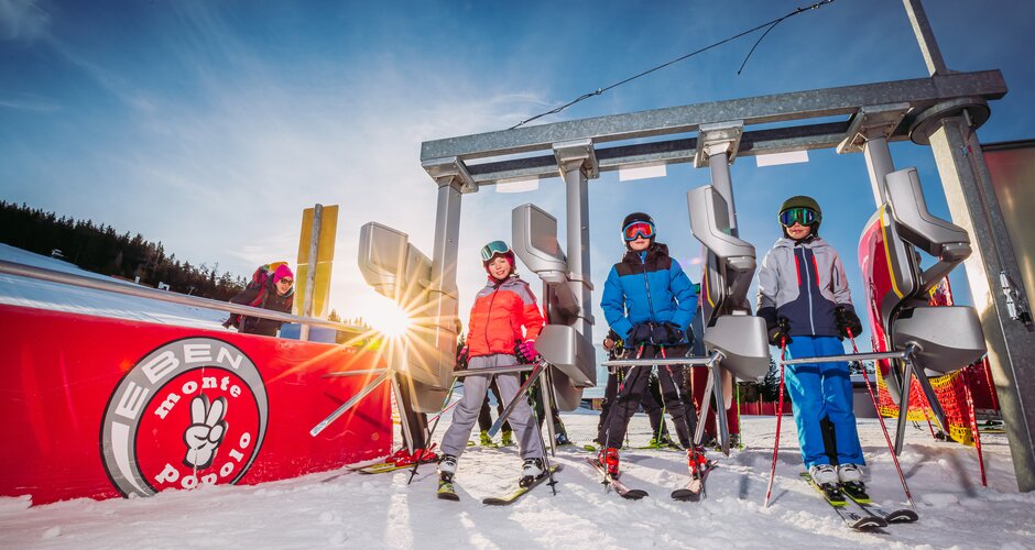 Three young people in ski clothes stand at the turnstile at the entrance to the lift. 