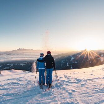 Two skiers enjoy the sunrise with view of snowy mountains and valleys