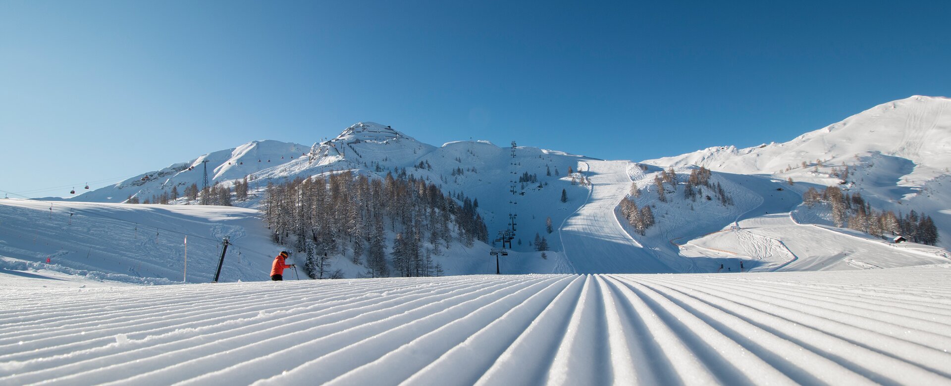 Freshly groomed piste with a view of the higher-lying piste landscape and the snow-covered surroundings