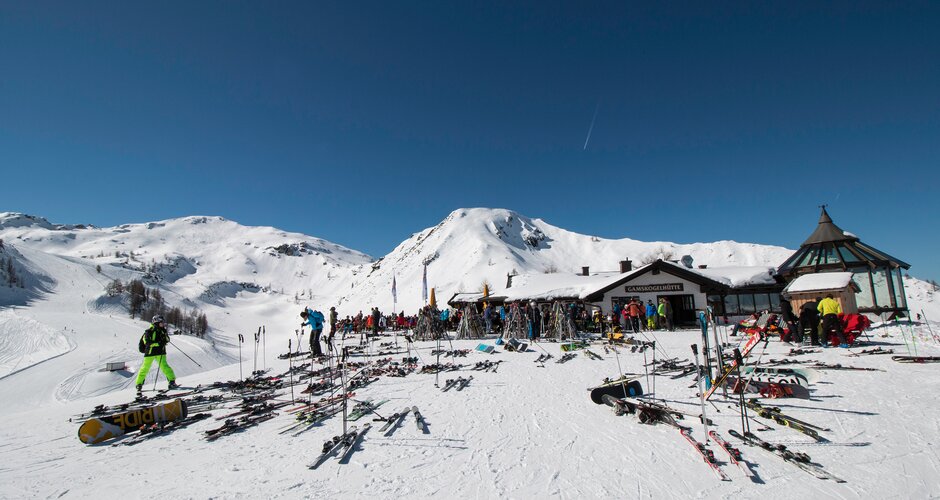Gamskogelhütte with many skis and snowboards, people enjoying the sun, mountain panorama