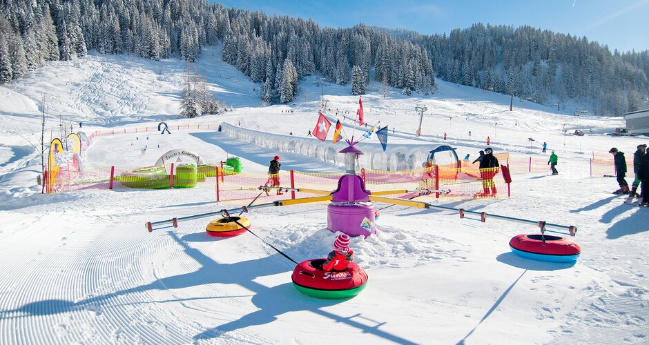Kids in tubing carousel on snow playground with magic carpet and course in Zauchensee
