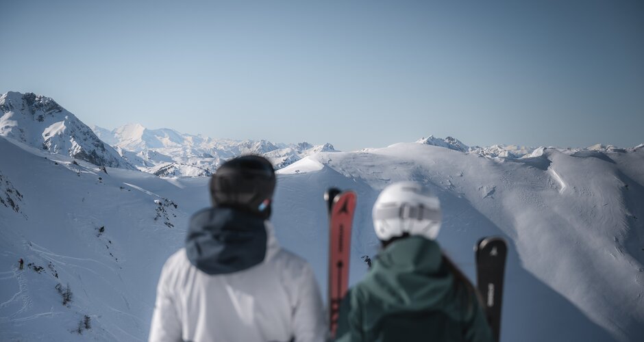 Two skiers with skis facing snowy mountains and wide panorama at Zauchensee
