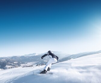 A skier rides a perfectly groomed slope with expansive mountain views.