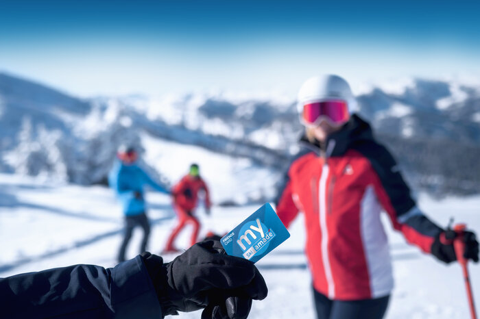 Hand mit schwarzem Skihandschuh hält eine blaue my Ski amadé Friends Card im Skigebiet
