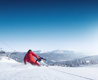 Two skiers in red and black outfits ski energetically down a slope