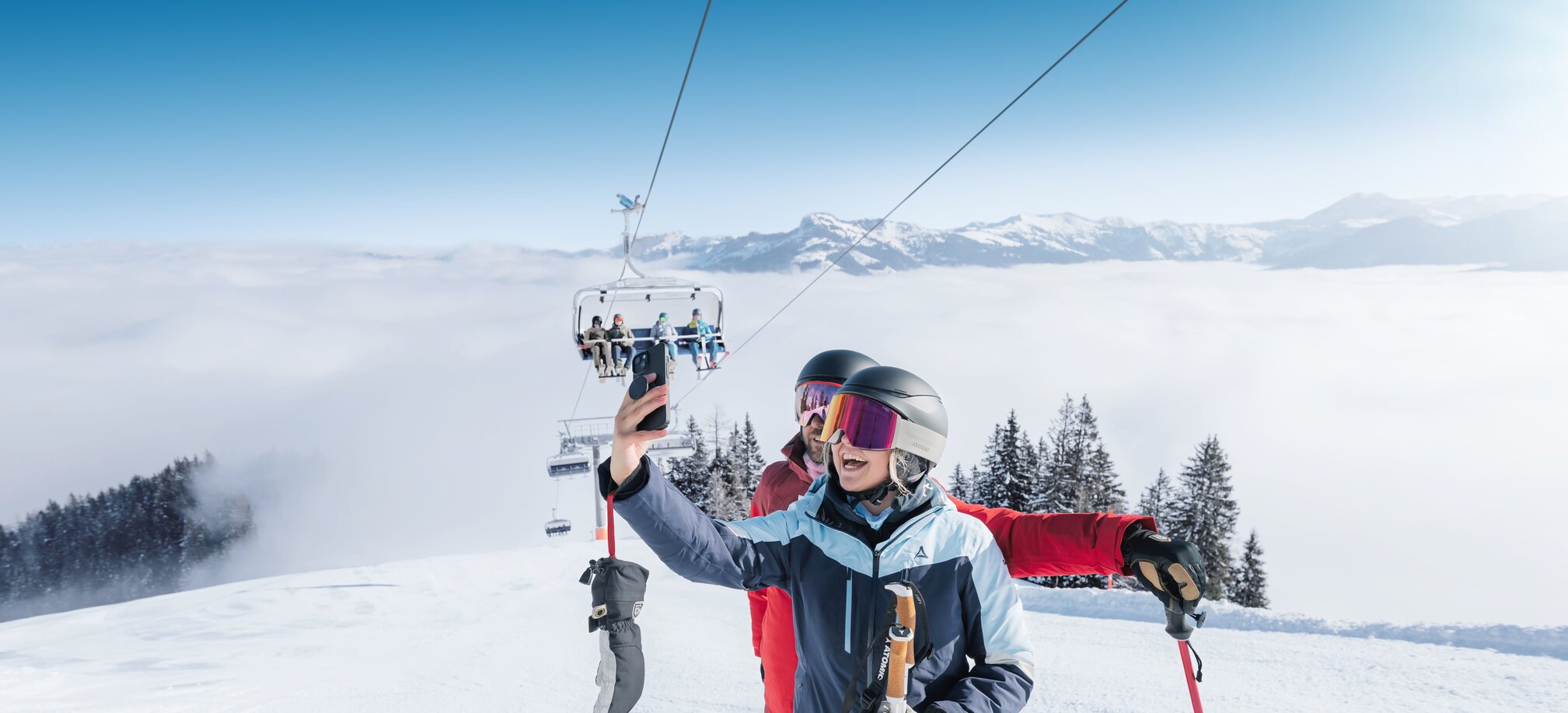 Two skiers take a selfie on sunny slope with chairlift and mountain view in Ski amadé