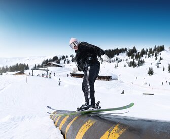 Young female skier balances on yellow-black rail in snow park on a sunny winter day