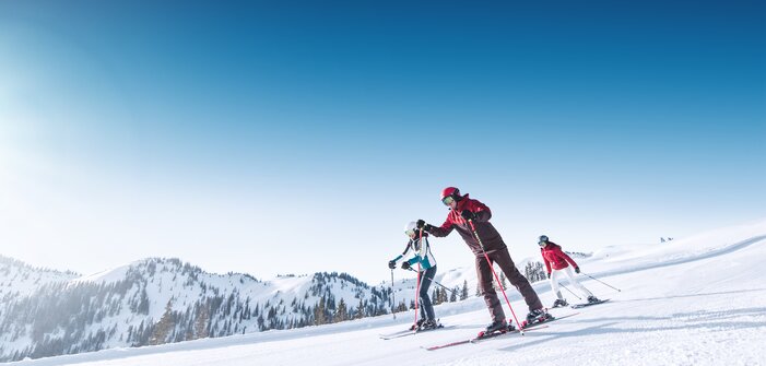Three skiers skiing down a wide, perfectly groomed slope together.