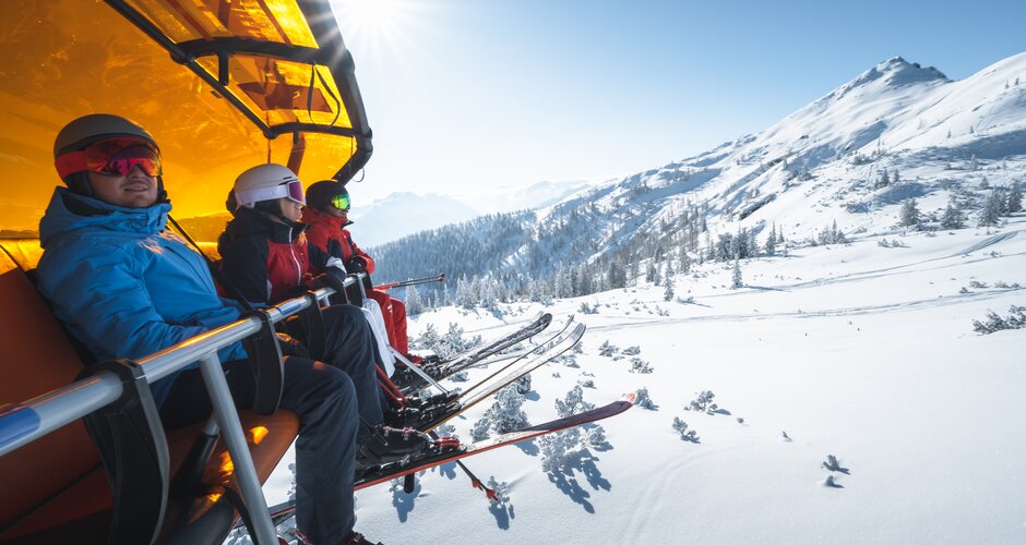 Four skiers sitting in a chairlift with an orange snow cover | © Ski amadé