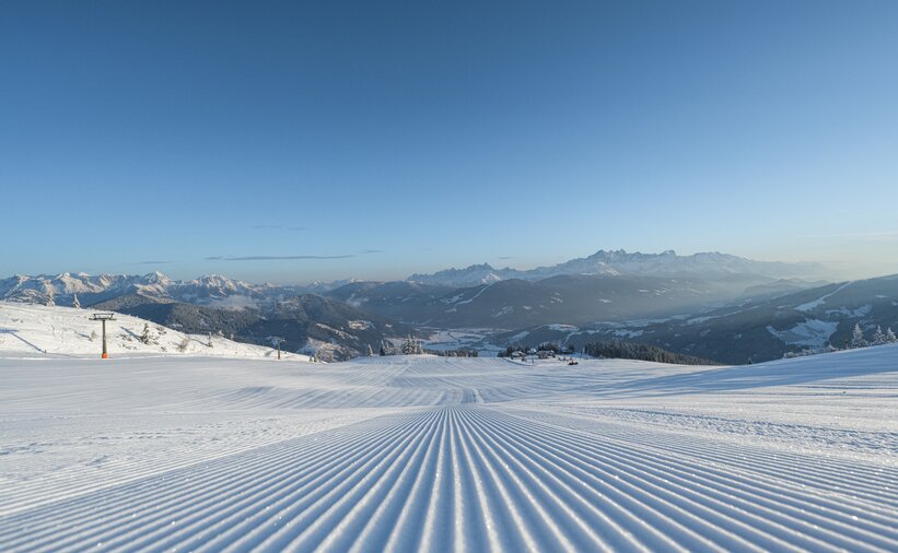 A freshly groomed ski slope with a view of snow-covered mountains. | © Ski amadé