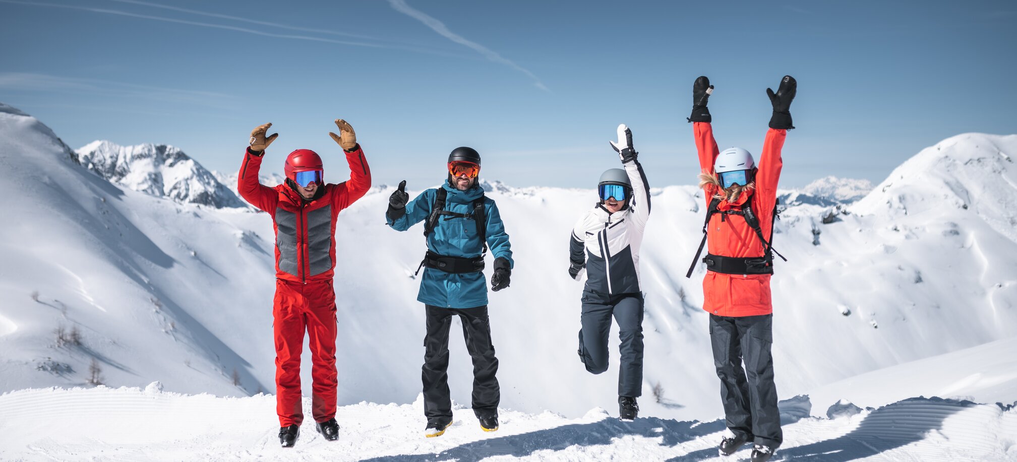 Vier Skifahrer springen gleichzeitig in die Luft, Schneeberge und Sonne im Hintergrund