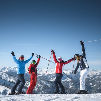 Vier Freunde in Skiausrüstung stehen auf der Piste und Strecken die Arme freudvoll in die Höhe. | © Ski amadé
