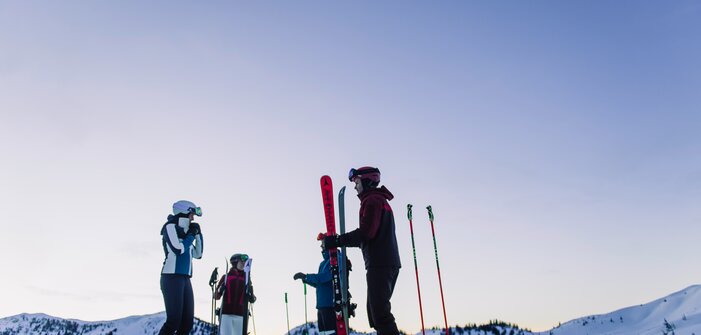 Four skiers stand on a snowy slope under a violet sky. | © Ski amadé