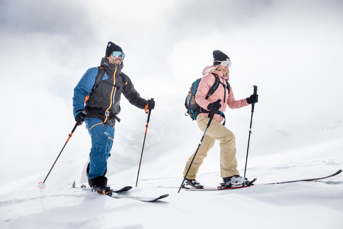 Two ski tourers ascend side by side through fresh snow under a cloudy alpine sky | © Harald Steiner