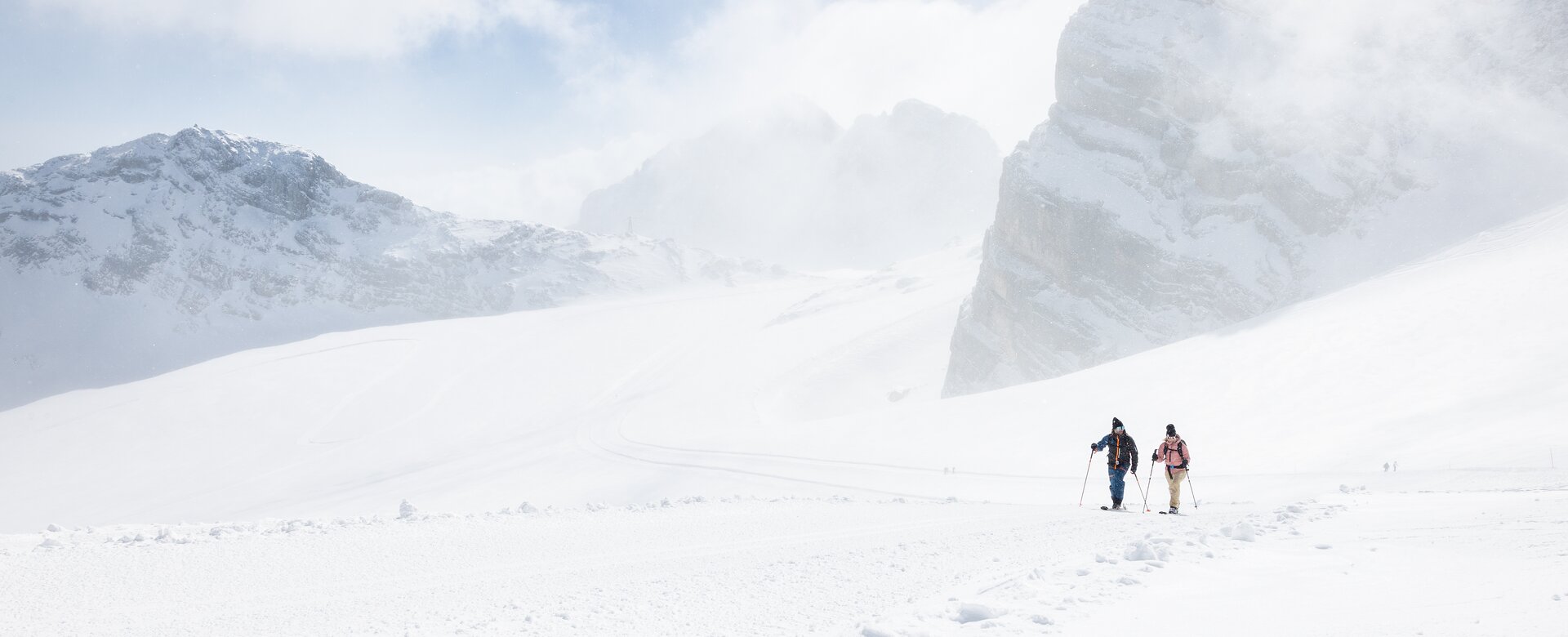 Two ski tourers walk side by side through snowy mountain landscape with rocky peaks | © Harald Steiner
