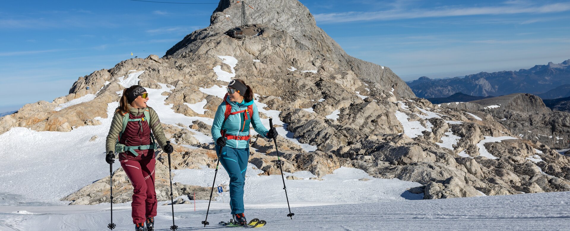 Two women ski touring in sunny weather with rocky mountain peak in the background | © H. Steiner