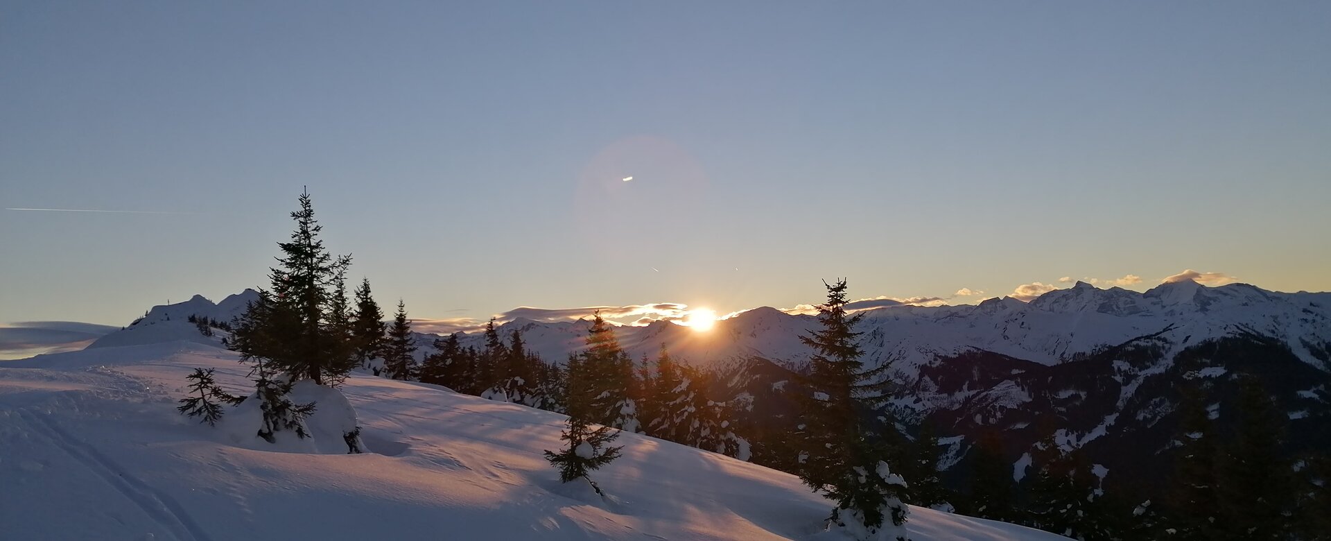 Winterlandschaft mit verschneiten Bäumen und Sonne hinter Bergkette bei Dorfgastein