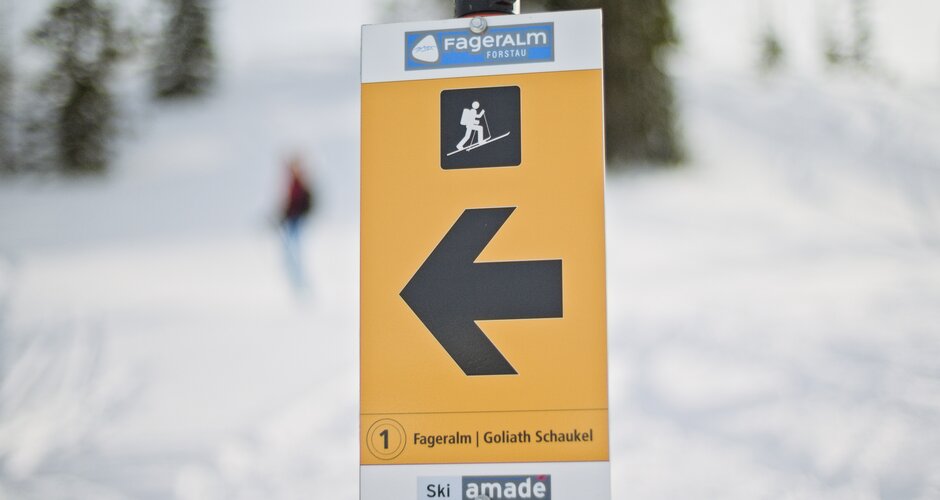 Yellow ski touring sign with arrow to Goliath swing on Fageralm in snowy landscape