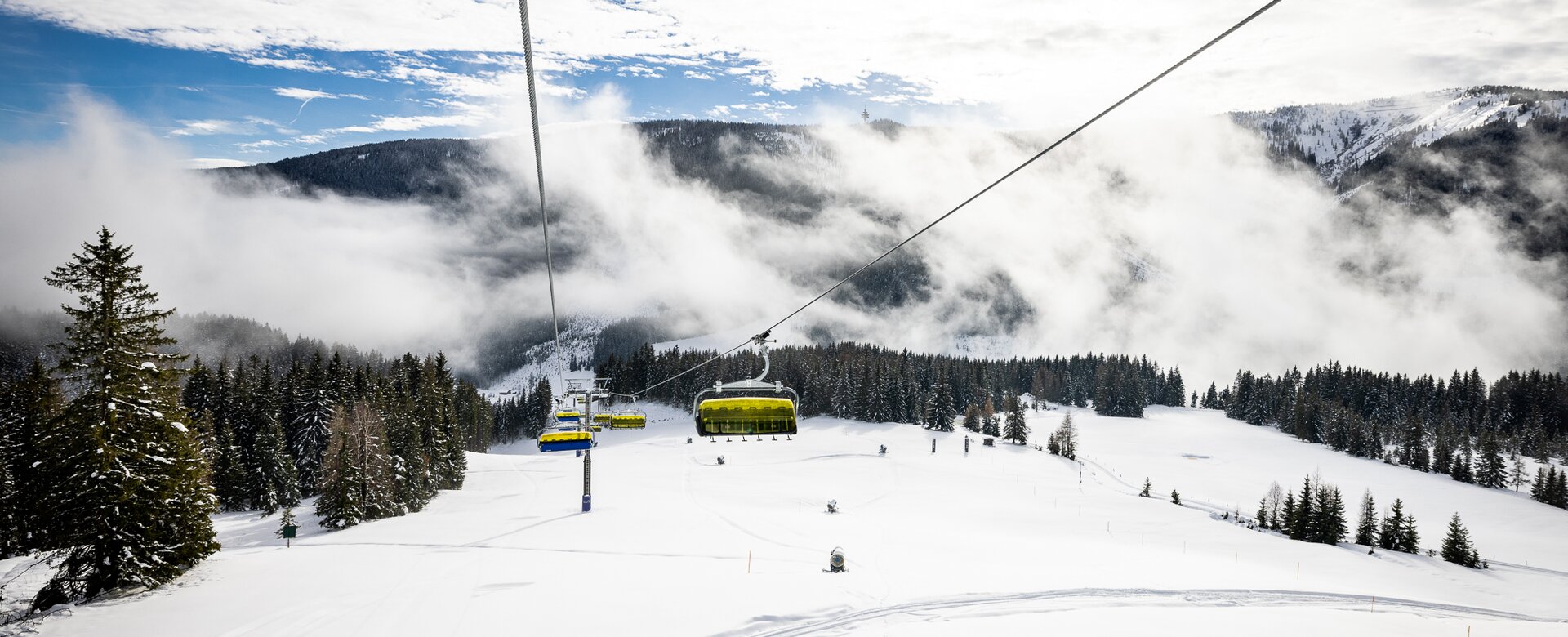 Gelber Sessellift fährt über verschneite Pisten und Wald in nebeliger Winterlandschaft | © filzmoos.ski