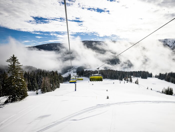 Gelber Sessellift fährt über verschneite Pisten und Wald in nebeliger Winterlandschaft | © filzmoos.ski