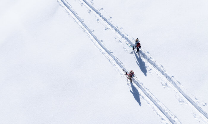 Zwei Pistentourengeher mit Stöcken auf verschneiter Spur bei Sonne auf der Planai unterwegs | © Josh Absenger