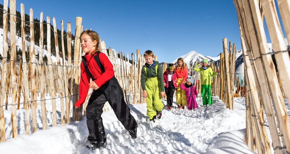 Group of children happily running through snowy course with wooden fences in the Gasti Kinderpark in Gastein | © Gasteiner Bergbahnen AG