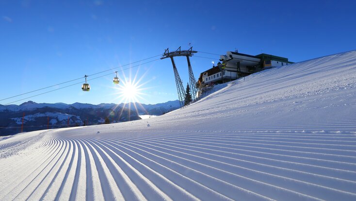 Die aufgehende Sonne bestrahlt die frisch präparierte Piste und die Kabinenbahn fährt darüber hinweg | © Tourismusverband Großarltal