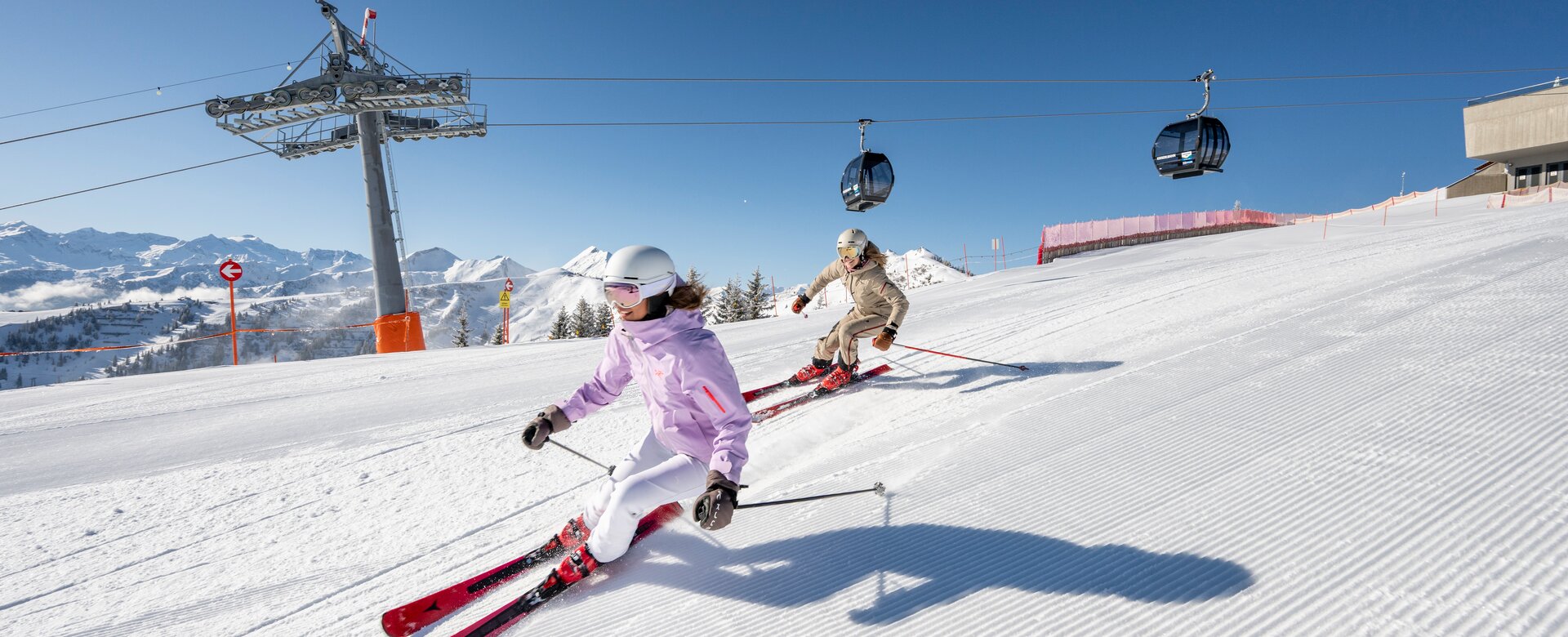 Two people skiing on a groomed alpine slope under bright sunshine | © Lorenz Masser