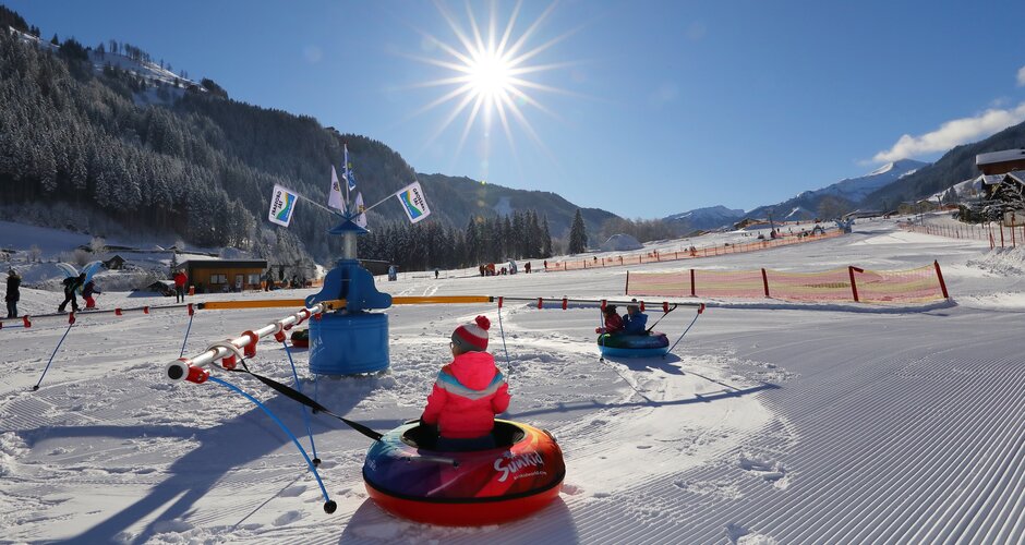 Kids ride tubing carousel on the snowy adventure meadow in Grossarltal under bright sunshine