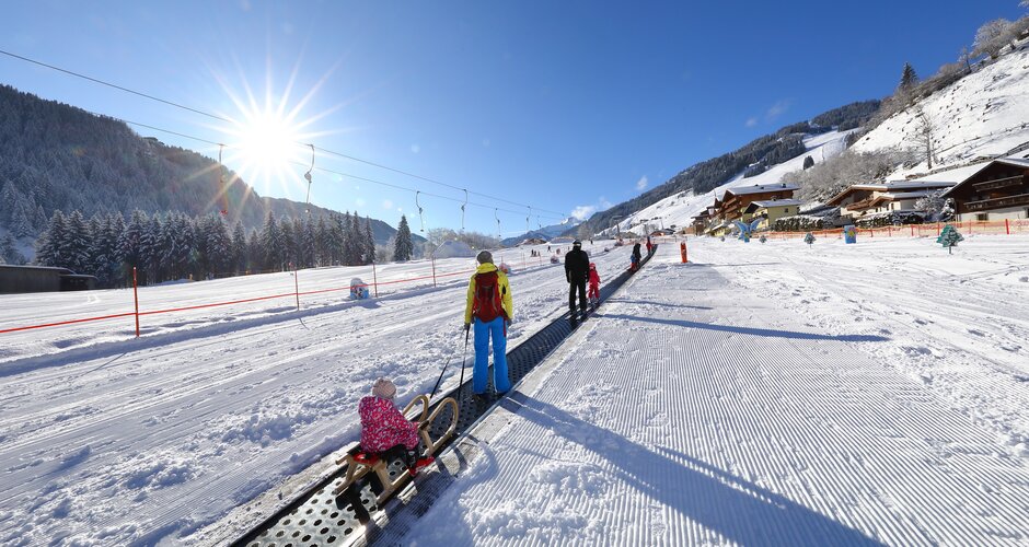 Families at the Fischbacher adventure meadow in Grossarl with sled and conveyor belt in the sun
