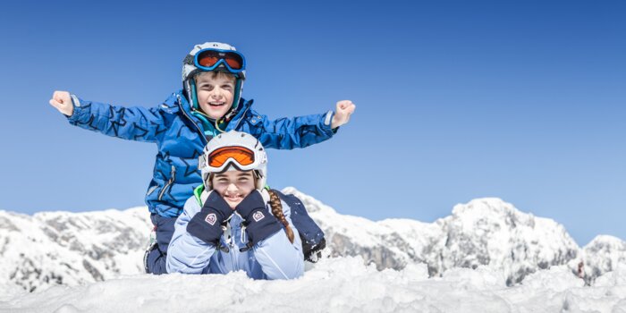Two children in ski gear playing in the snow with snowy Alpine mountains behind | © Felsch Fotodesign