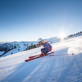 A skier in athletic pose on freshly groomed slope in bright winter sun
