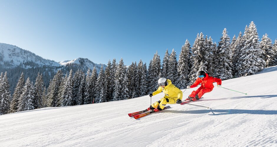 Two skiers in yellow and red outfits skiing in parallel on a snowy slope | © Hochkönig Tourimus GmbH