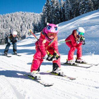 Two children crouch down on their skis and ski along a tow path with their parents following right behind them | © Salzburger Sportwelt, Christian Schartner