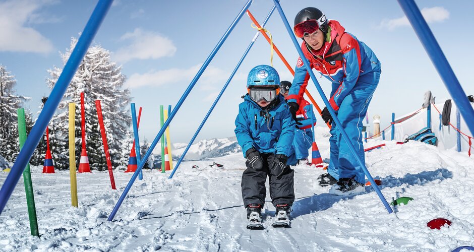 Ski instructor guides toddler with helmet through snowy course in kids' area in Alpendorf | © Armin Walcher, Skischule Alpendorf
