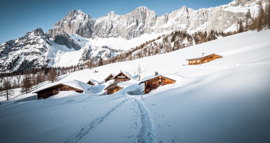 Footprints lead to snow-covered alpine huts below Dachstein mountains in wintry alpine landscape | © Mathäus Gartner