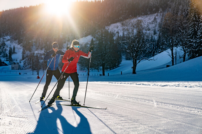 Two cross-country skiers in sportswear ski Ramsau trail in low sun on freshly groomed winter track | © Christine Höflehner